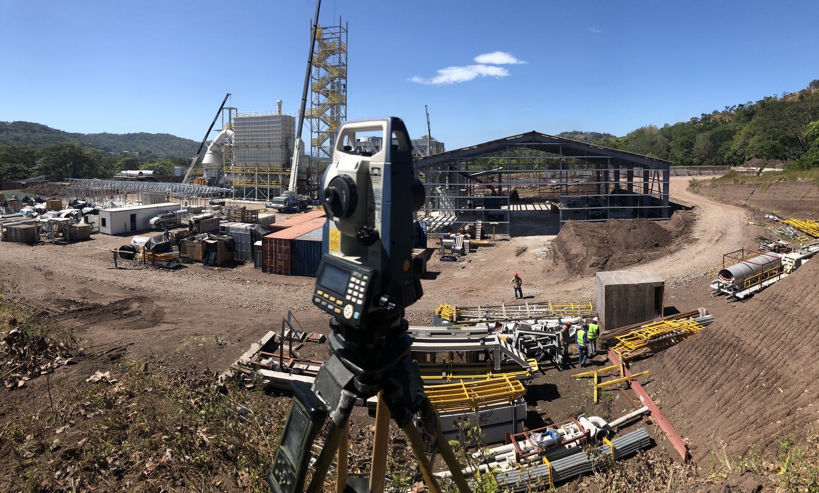 Estación total montada en trípode frente a una obra industrial en construcción
